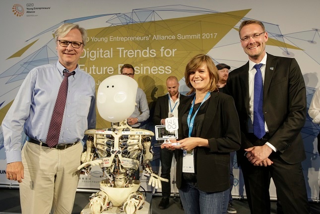 Ventura TRAVEL receives WE DO DIGITAL award at the G20 Young Entrepreneur Summit. Hester from the Marketing Team stands on stage with represntatives of the DIHK and a robot.